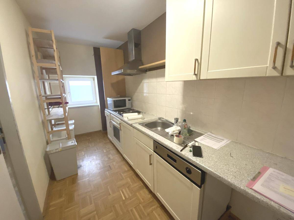 Funktionale Küche mit weißen Schränken, Einbaugeräten und Parkettboden.