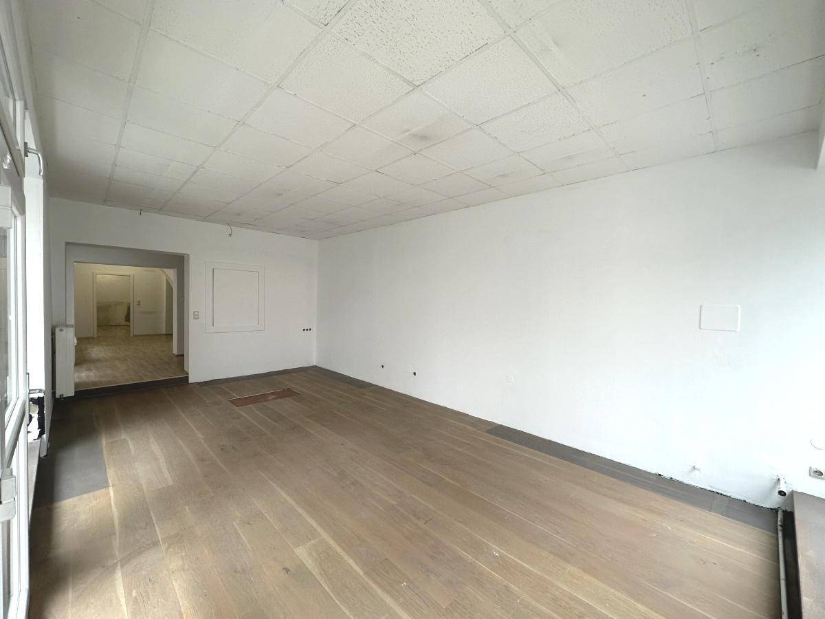 Geräumiger, leerer Geschäftsraum mit hellem Holzboden und einer Decke mit Akustikplatten.