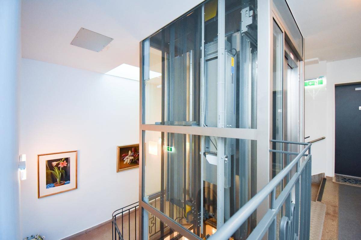 Moderner Glasaufzug im Treppenhaus, der barrierefreien Zugang zu den Etagen ermöglicht.
