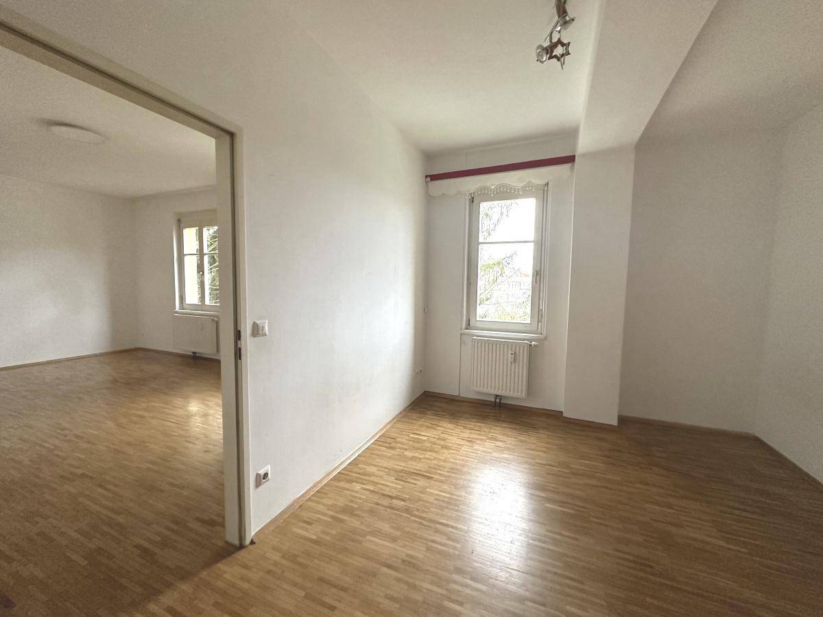 Lichtdurchflutetes Zimmer mit Parkettboden und Zugang zu einem weiteren hellen Raum.