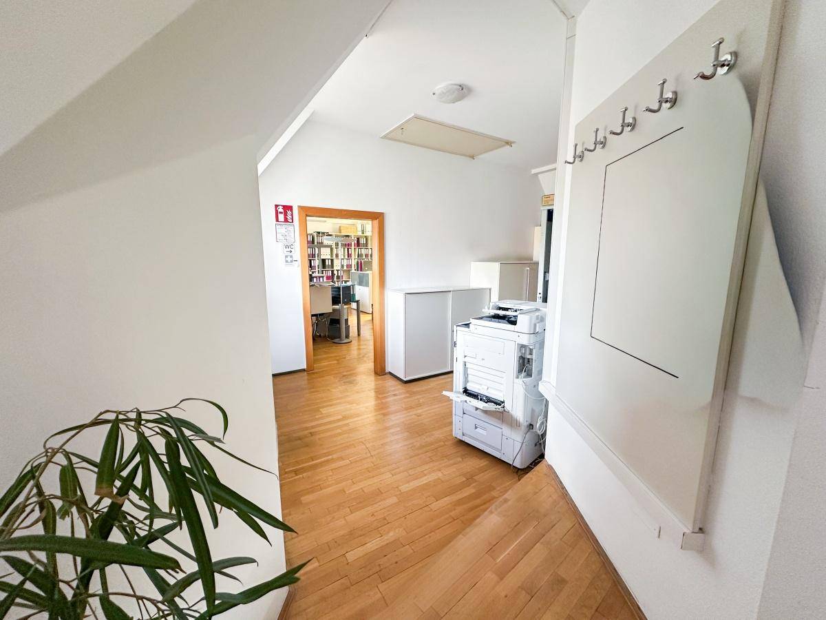 Heller Flur mit Holzfußboden, Garderobe und Zugang zu weiteren Büroräumen.