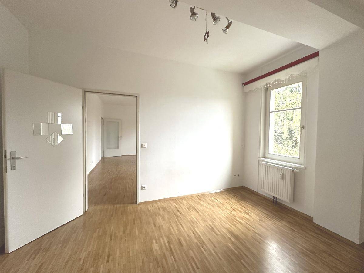 Helles Zimmer mit Parkettboden, weiß gestrichenen Wänden und Blick ins Grüne.