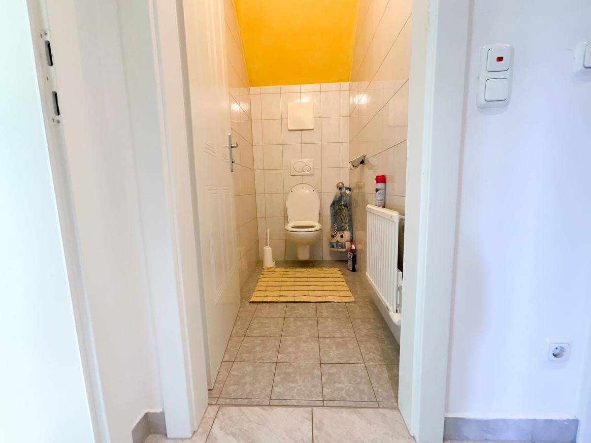 Kleines WC mit Fliesenboden, weiß gefliesten Wänden und gelber Decke.