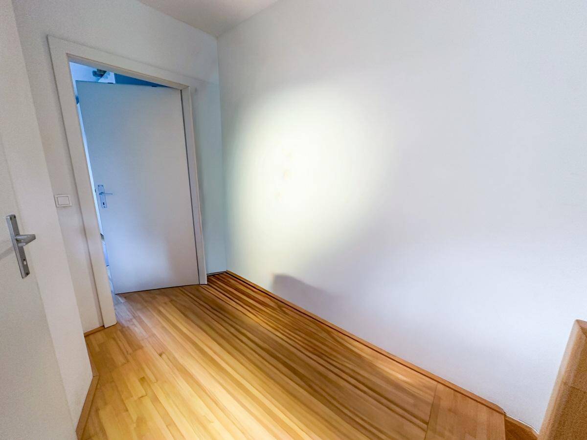 Heller Innenraum mit Holzboden und weißen Wänden, möglicherweise ein Durchgangsbereich.