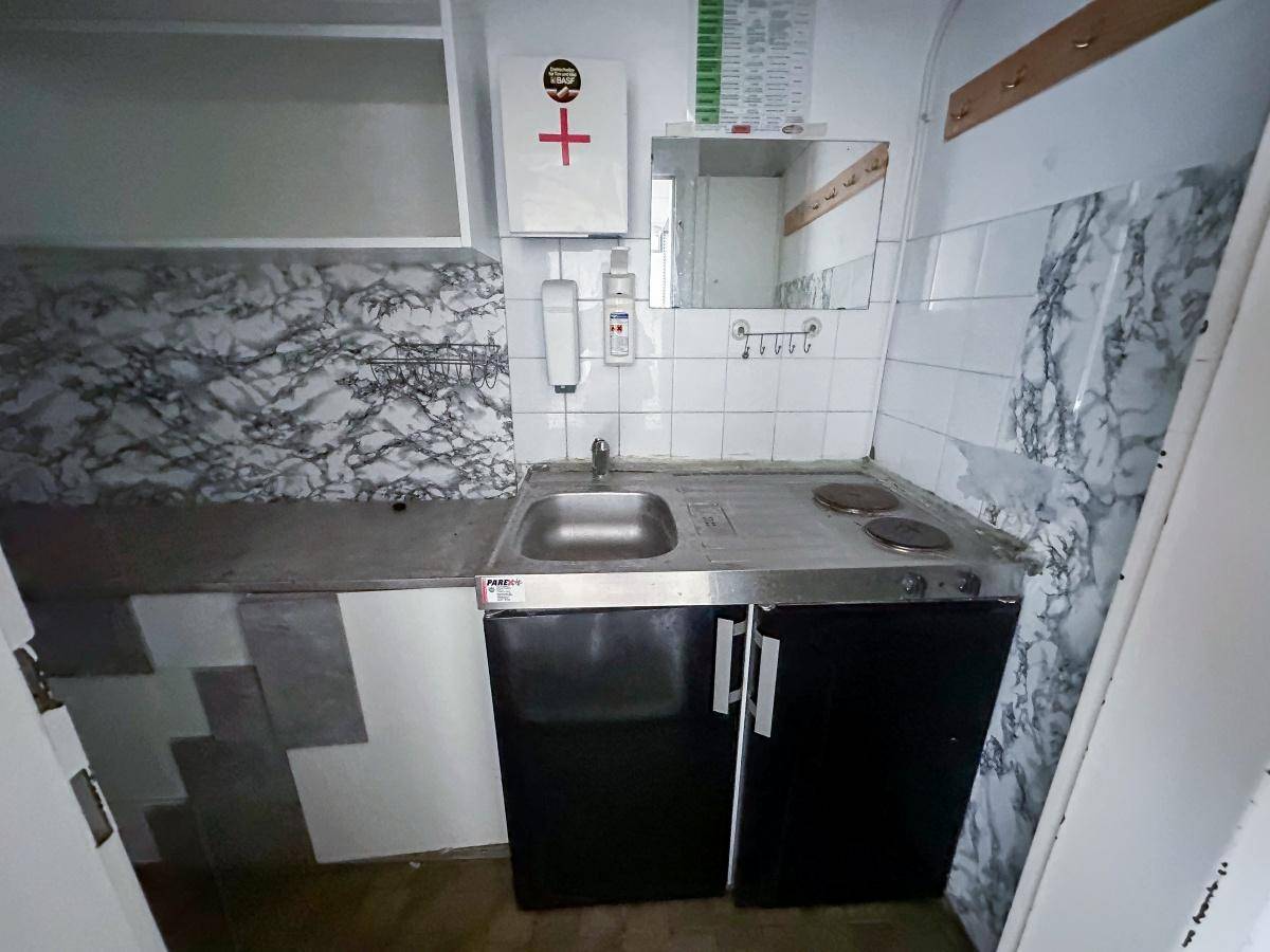Kleine, funktionale Küchenzeile mit Spüle, Kochplatten und Kühlschrank, ideal für eine Teeküche.