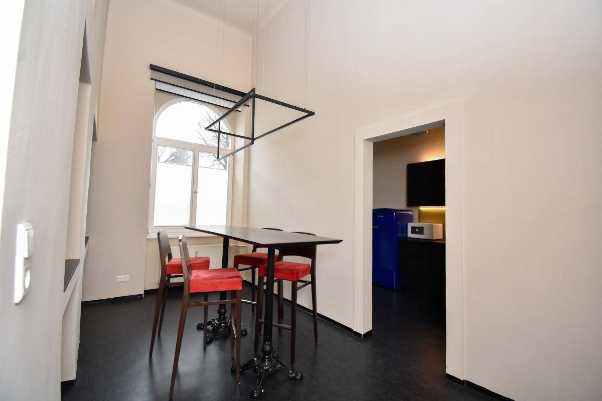 Kleiner Essbereich mit Stehtisch und roten Stühlen, angrenzend an eine moderne Küchenzeile mit blauem Kühlschrank.