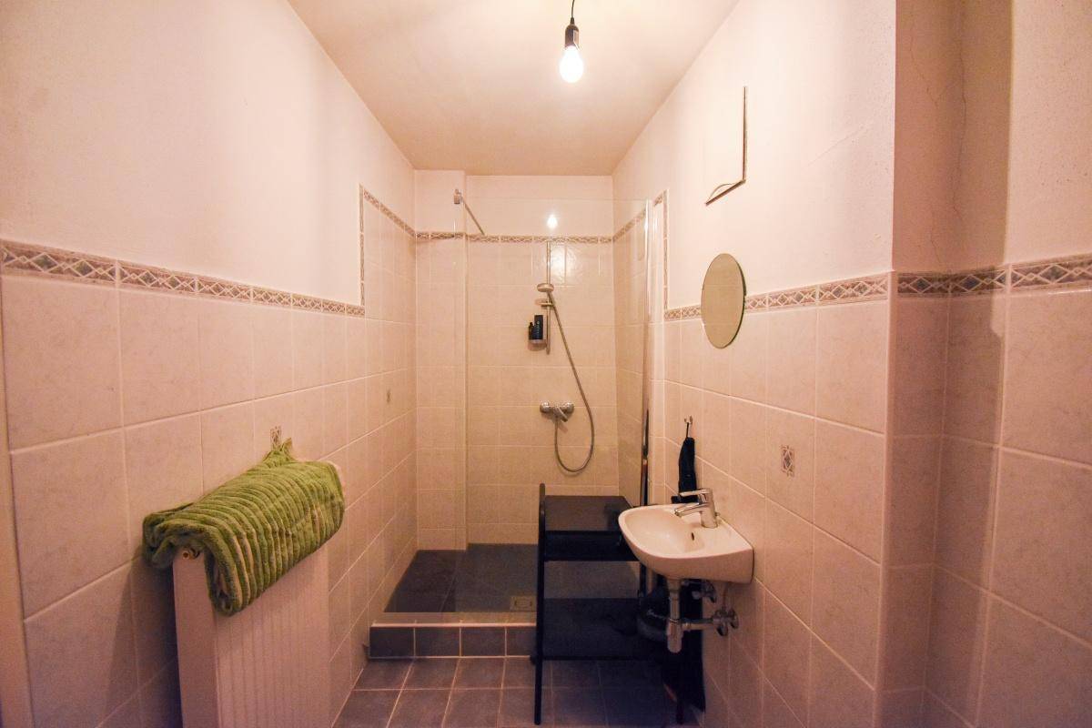 Helles Badezimmer mit hellen Fliesen, einer Duschkabine und einem Waschbecken mit Spiegel.