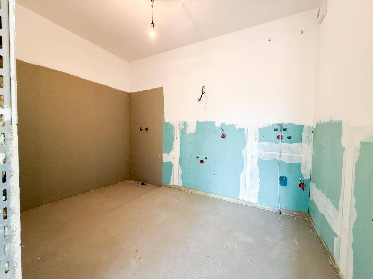 Küche im Rohbau mit vorbereiteten Anschlüssen für Geräte und unverputzten Wänden.