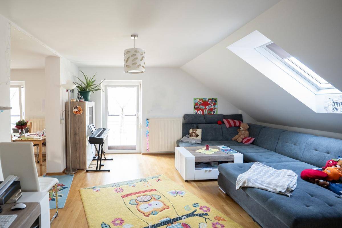 Helles Wohnzimmer im Dachgeschoss mit großem Sofa, Teppich und Balkonzugang.