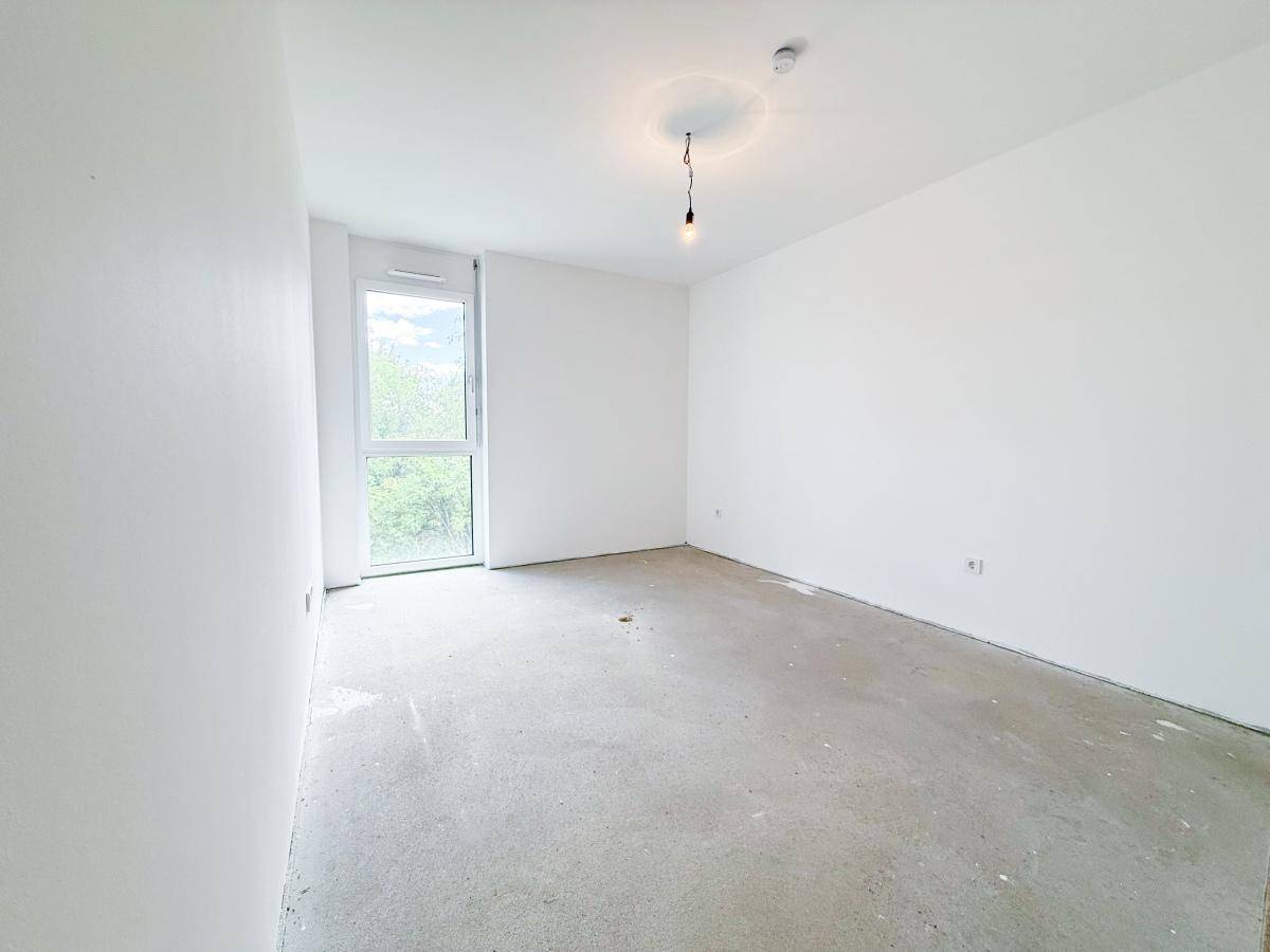 Unfertiges Schlafzimmer mit großen Fenstern, weiß gestrichenen Wänden und Betonboden.