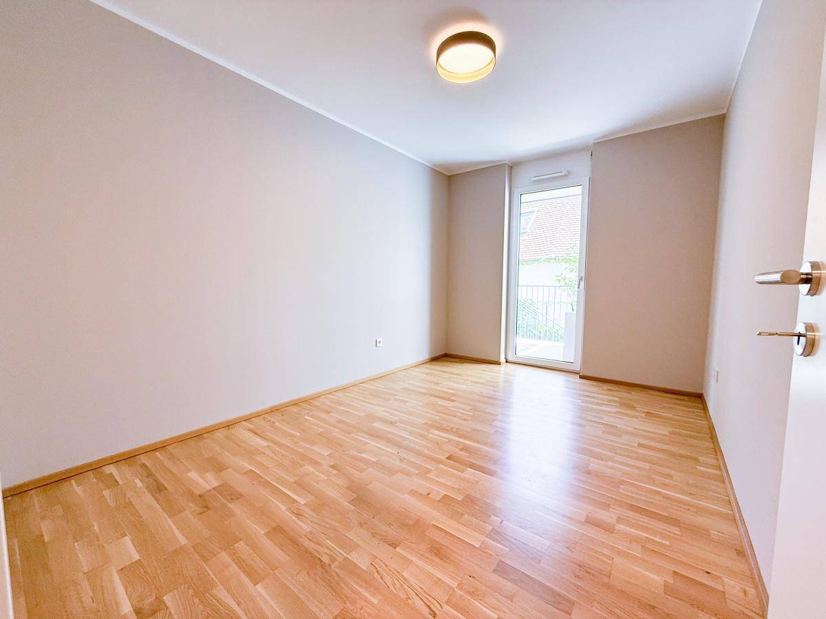 Helles Schlafzimmer mit Parkettboden und Zugang zu einem Balkon oder einer Terrasse, bereit zur Einrichtung.