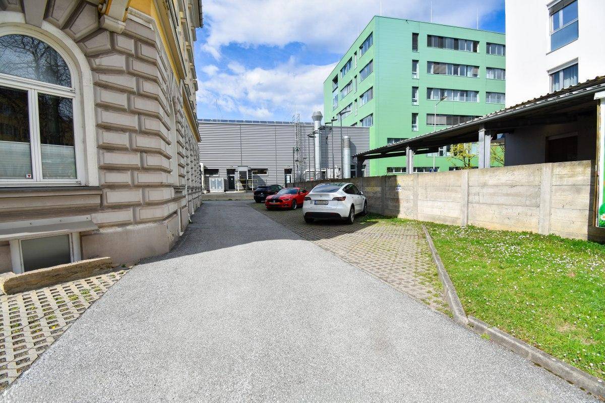 Zufahrt und Parkbereich neben dem Gebäude mit angrenzender Grünfläche.