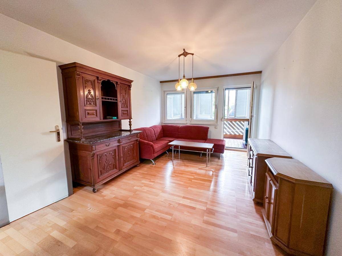 Gemütliches Wohnzimmer mit Holzparkett, rotem Ecksofa und traditionellen Holzmöbeln.