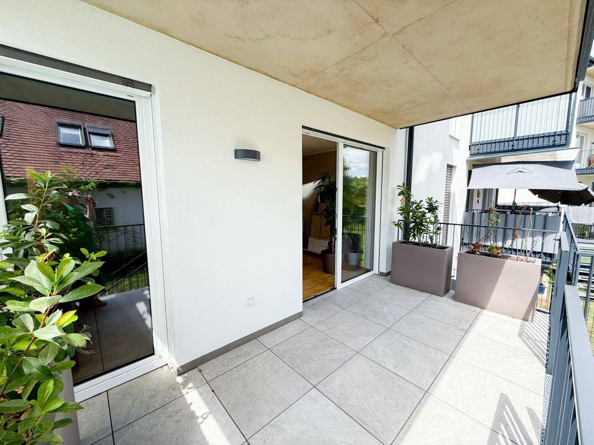 Heller Balkon mit Fliesenboden, Pflanzen und Blick auf die umliegenden Gebäude.