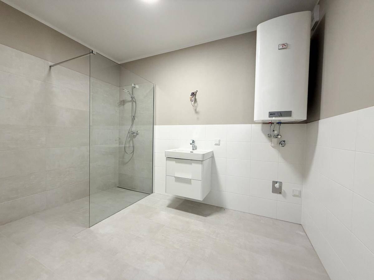 Geräumiges Badezimmer mit moderner begehbarer Dusche, Waschbecken und hellem Fliesenboden.