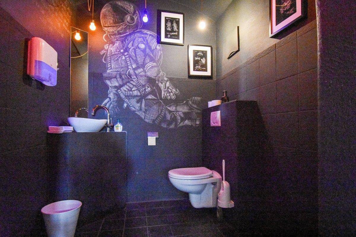 Modernes Gäste-WC mit dunklen Fliesen, Wand-WC und einem auffälligen Astronauten-Wandbild.