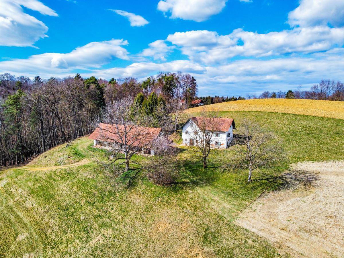 Panoramablick auf zwei ländliche Gebäude inmitten einer hügeligen Landschaft mit Wäldern.