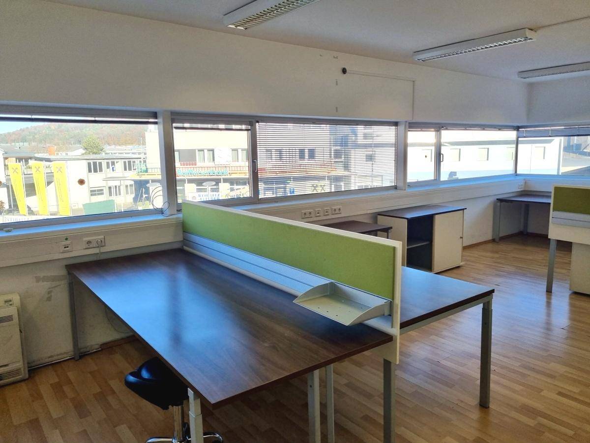 Büroraum mit Schreibtischen, grünen Trennwänden und Fenstern, die einen Blick auf die Stadt bieten.