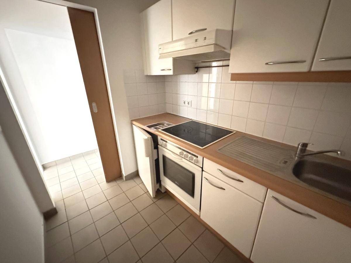 Kleine Einbauküche mit weißen Schränken, Holz-Arbeitsplatte und integrierten Geräten.