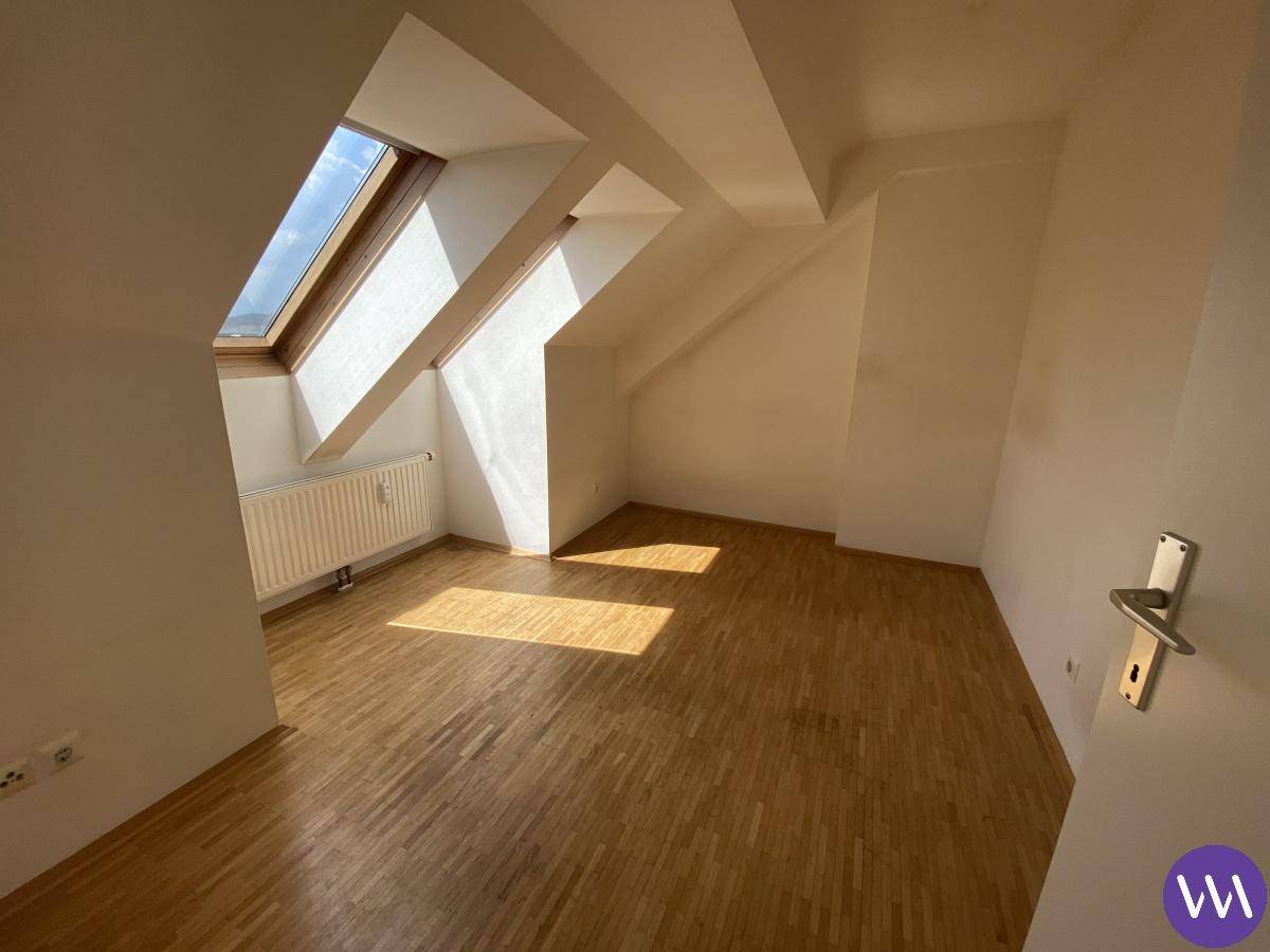 Helles Zimmer im Dachgeschoss mit Dachfenstern, Heizkörper und Parkettboden.