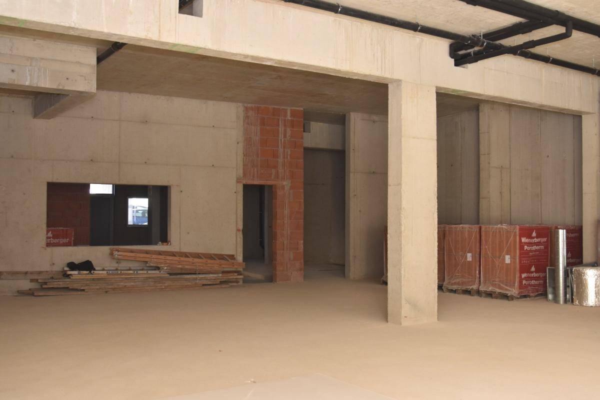 Großer Rohbau mit Betonwänden, einem Wanddurchbruch und gestapelten Baustoffen, bereit für den Ausbau.