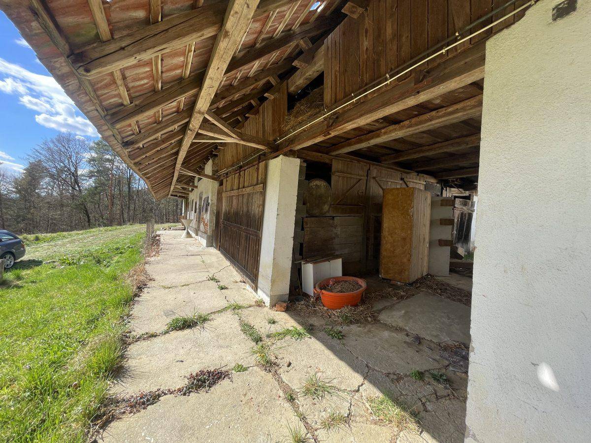 Überdachter Außenbereich eines alten Bauernhauses mit Holzbalken und Betonboden.