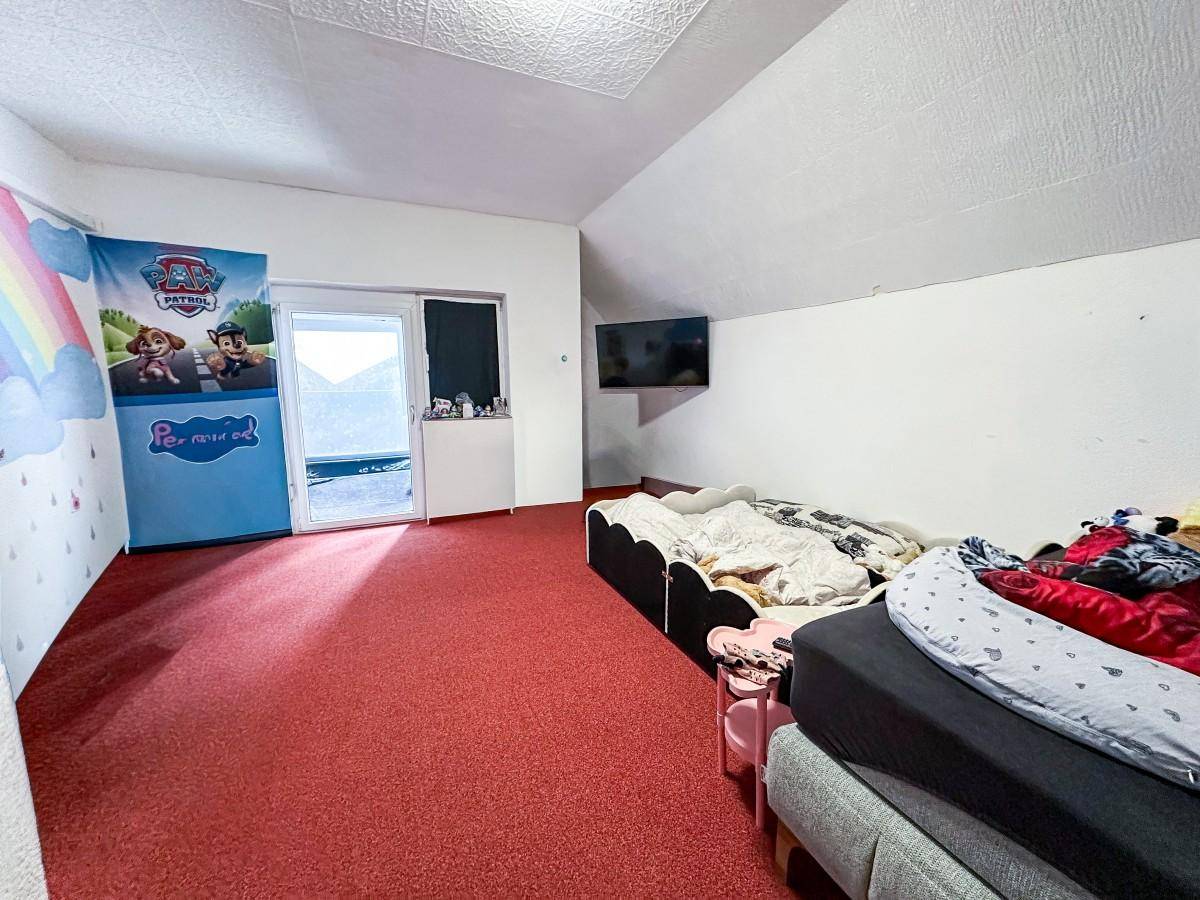 Kinderzimmer mit rotem Teppichboden, Dachschräge und Zugang zu einem kleinen Balkon.