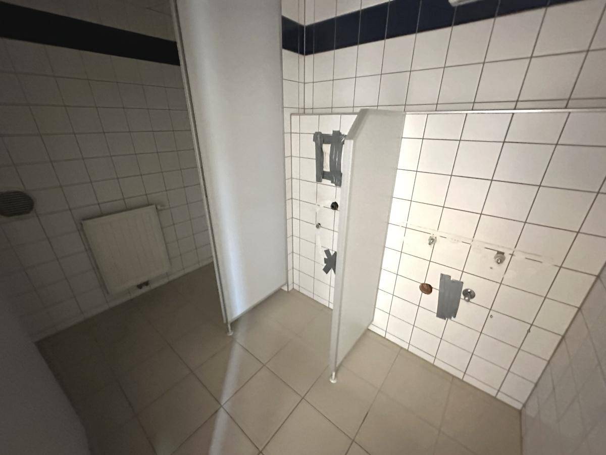 Toilettenbereich mit weißen Fliesen und Trennwänden, bereit für die Installation von Sanitärobjekten.
