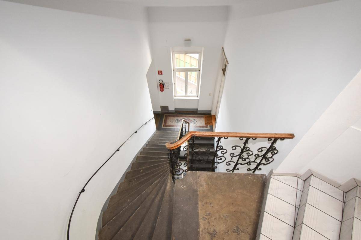 Treppenhaus von oben gesehen mit Steinstufen, Geländer und Fenster auf halber Höhe.