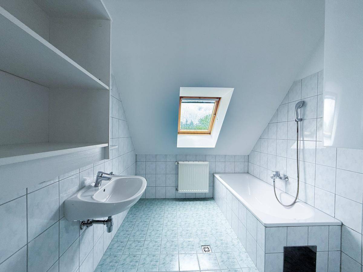 Badezimmer mit hellblauen Fliesen, Badewanne, Waschbecken und einem Dachfenster für natürliches Licht.