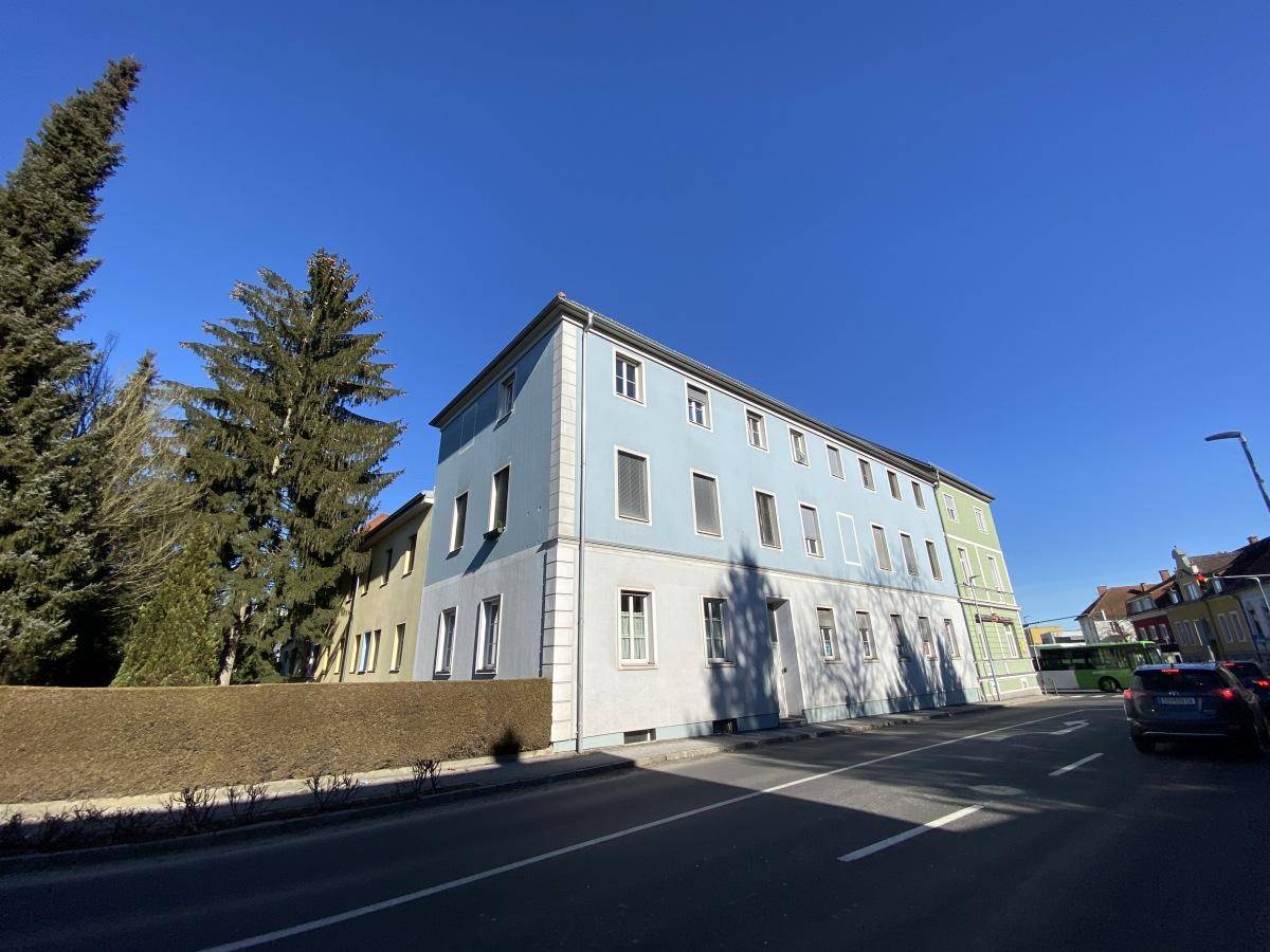 Ansicht des Gebäudes von der Straße mit blauer und grüner Fassade und hohen Bäumen.