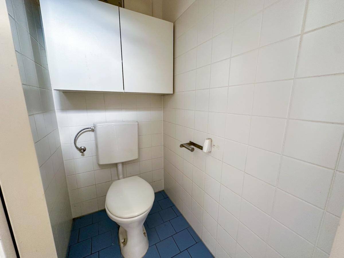 Kleines Gäste-WC mit weiß gefliesten Wänden, blauen Bodenfliesen und wandmontierter Toilette.