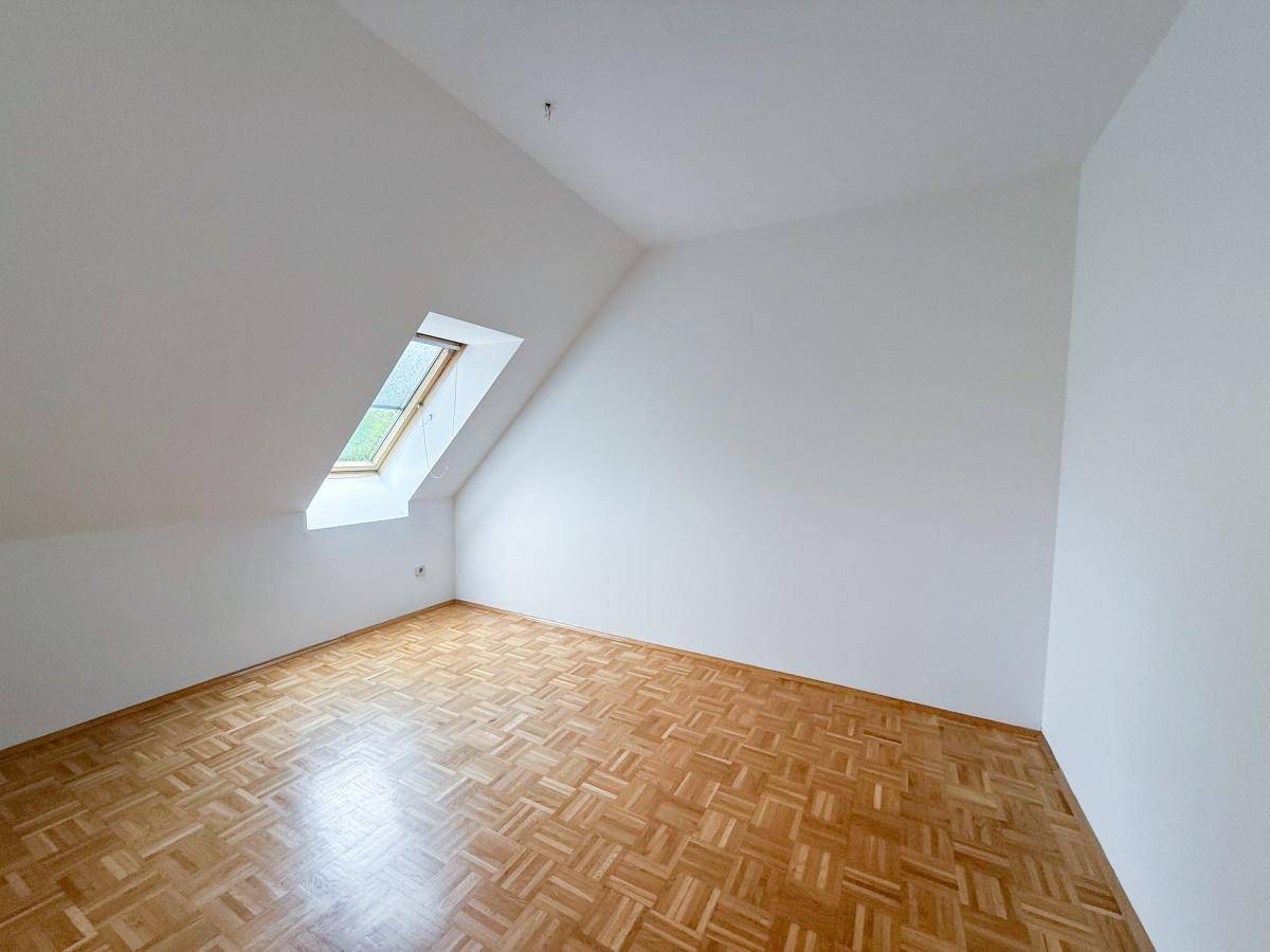 Helles Schlafzimmer mit Parkettboden, weißen Wänden und einem schrägen Dachfenster für viel Tageslicht.