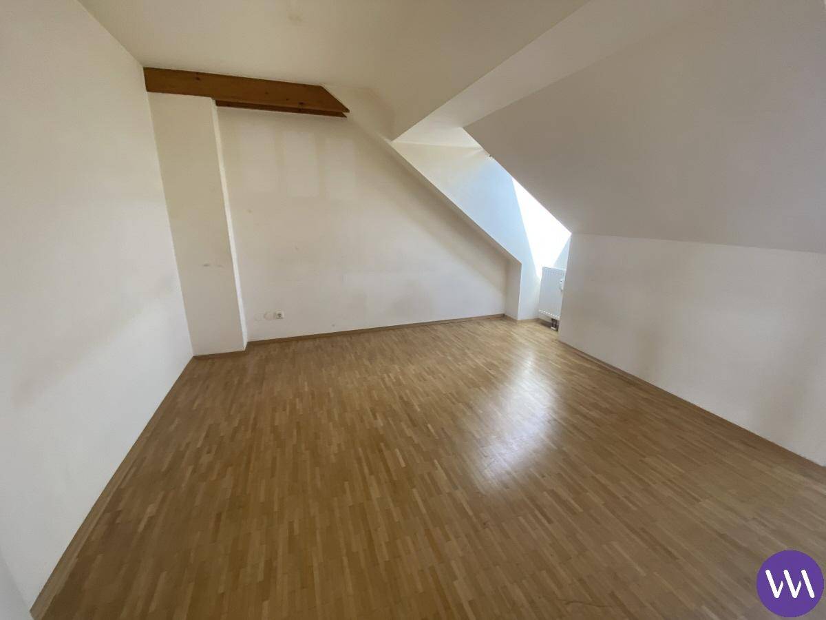 Leeres Zimmer im Dachgeschoss mit Holzbalken und Parkettboden, ideal als Schlafzimmer.
