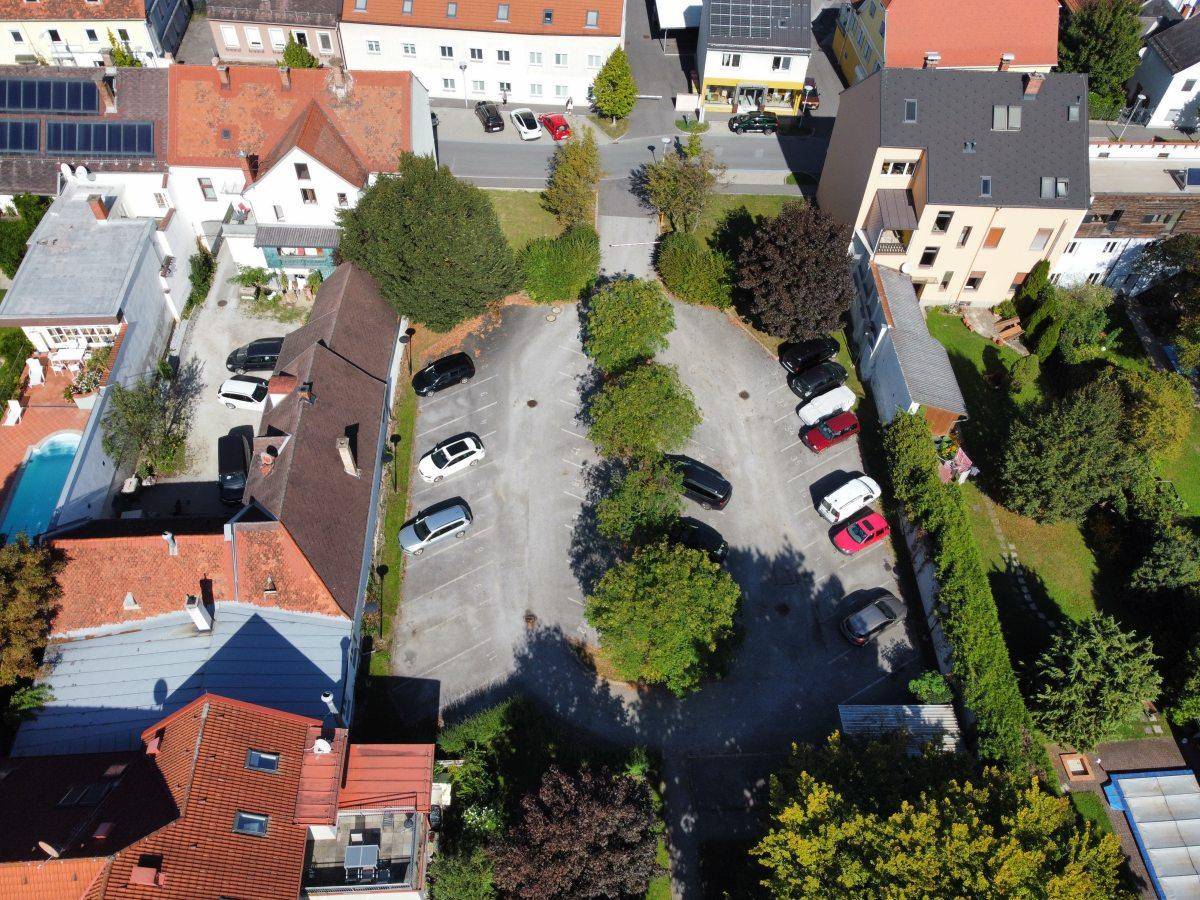 Übersicht aus der Vogelperspektive auf einen Parkplatz mit umliegenden Häusern und Bäumen.