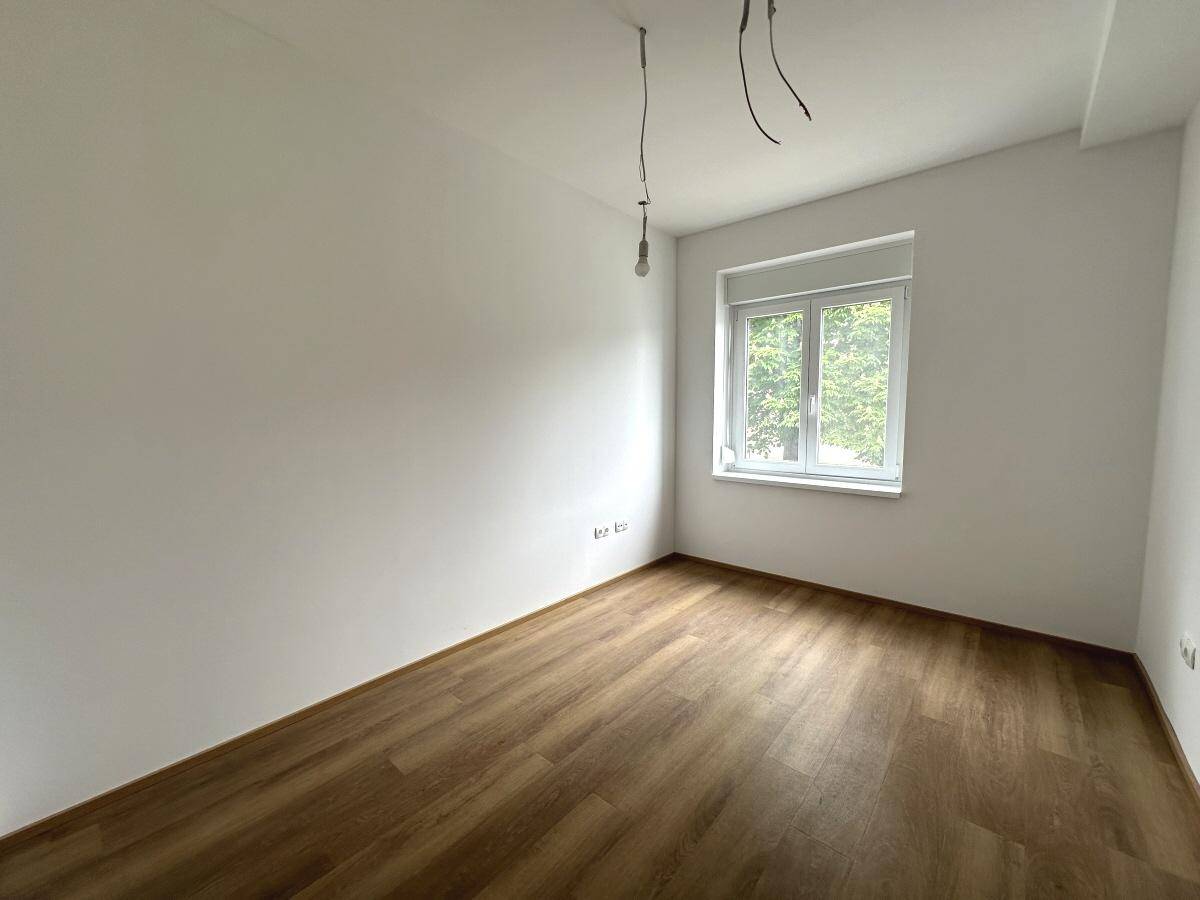 Leeres Schlafzimmer mit Laminatboden und einem Fenster, das viel Tageslicht hereinlässt.