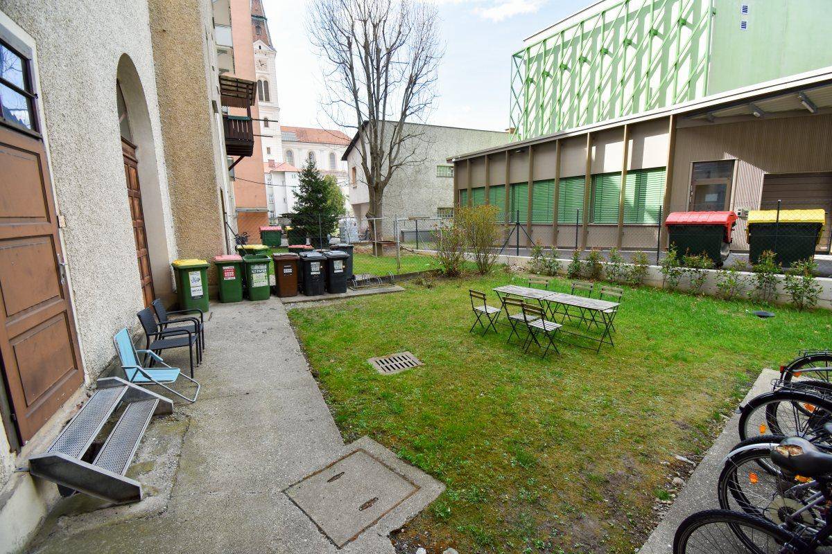 Gemeinschaftlicher Gartenbereich mit Rasenfläche, Sitzgelegenheiten und Mülltonnen.
