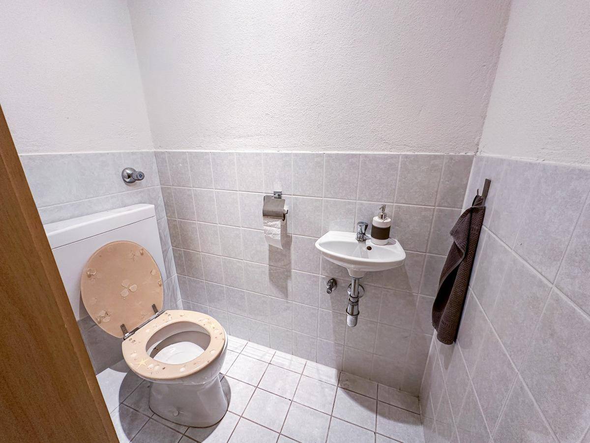 Kleines Gäste-WC mit Toilette, Waschbecken und hellen Wandfliesen.