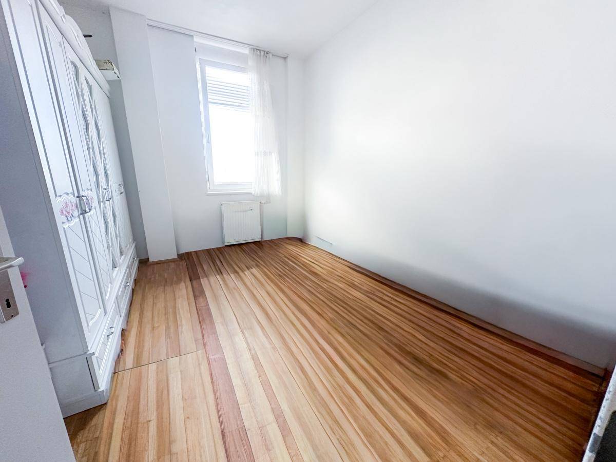Helles Schlafzimmer mit Parkettboden, weißem Kleiderschrank und Fenster.