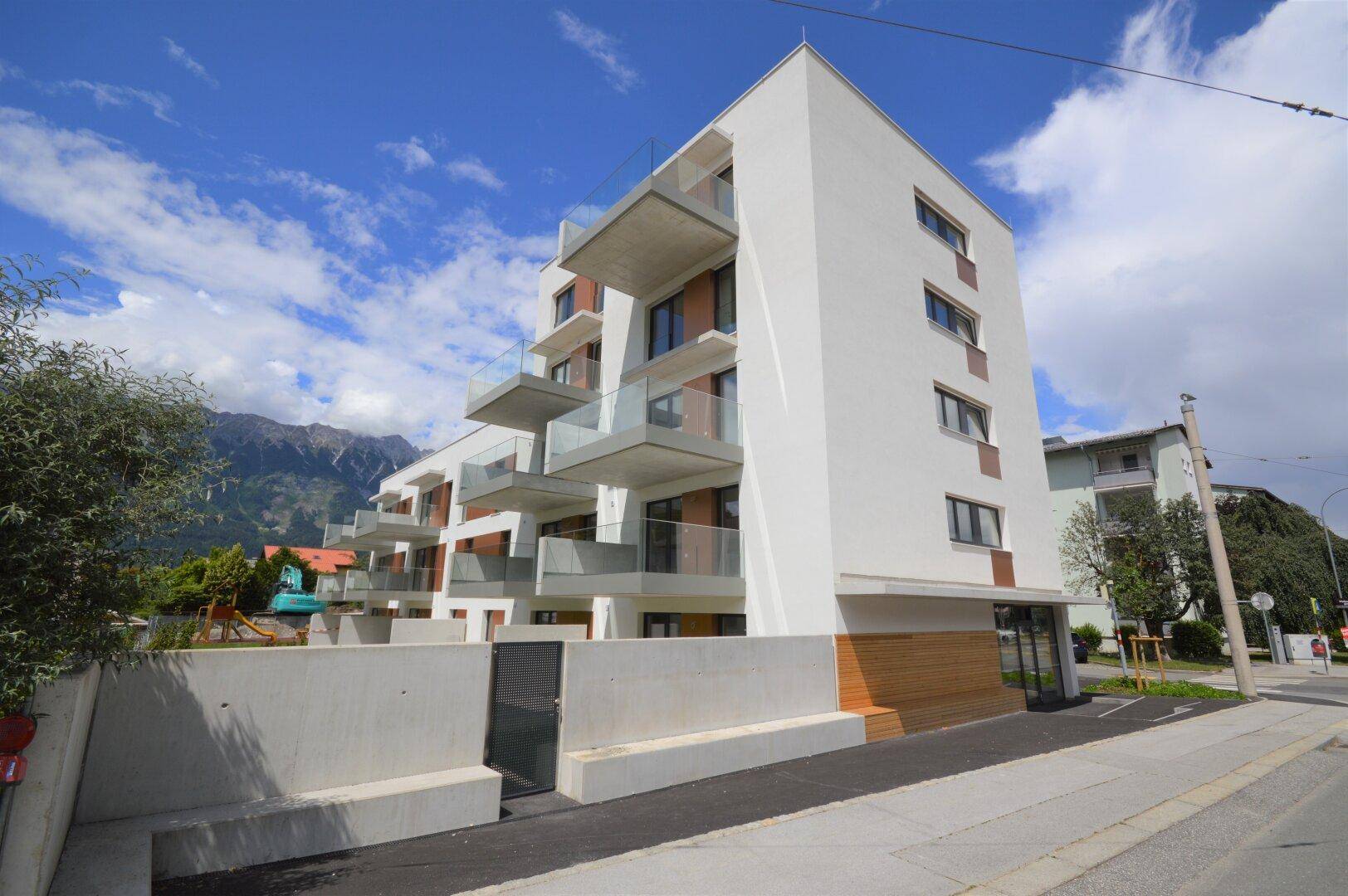 Modernes Mehrfamilienhaus mit mehreren Balkonen und einer klaren Architektur vor einer beeindruckenden Bergkulisse.
