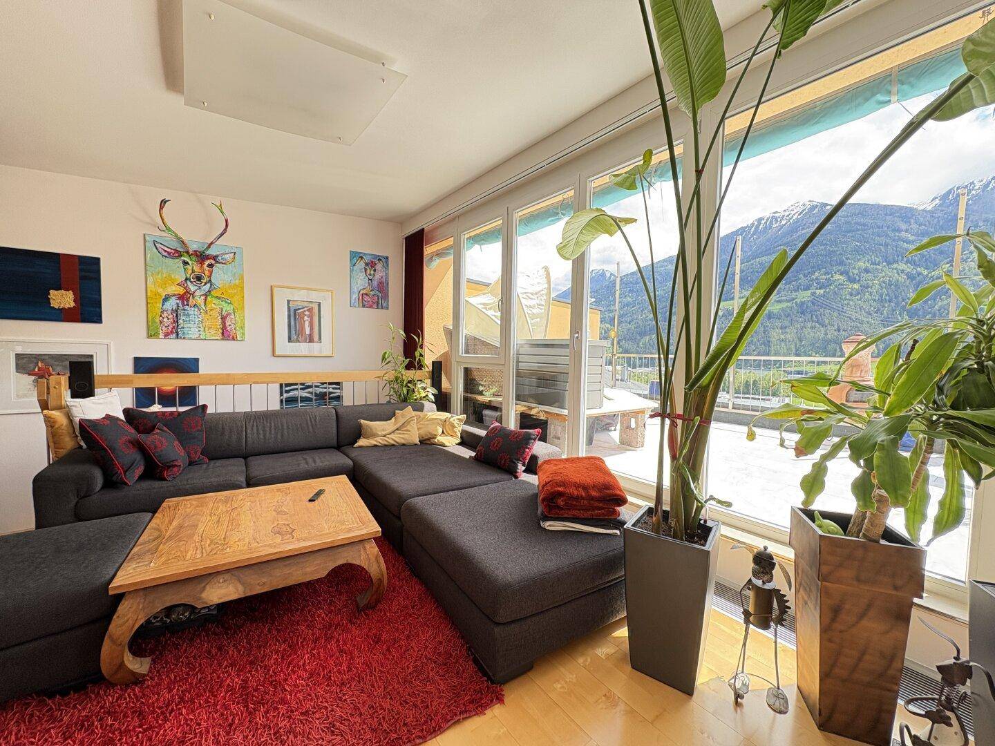 Helles Wohnzimmer mit großem Sofa, Holzboden und bodentiefen Fenstern mit Bergblick.