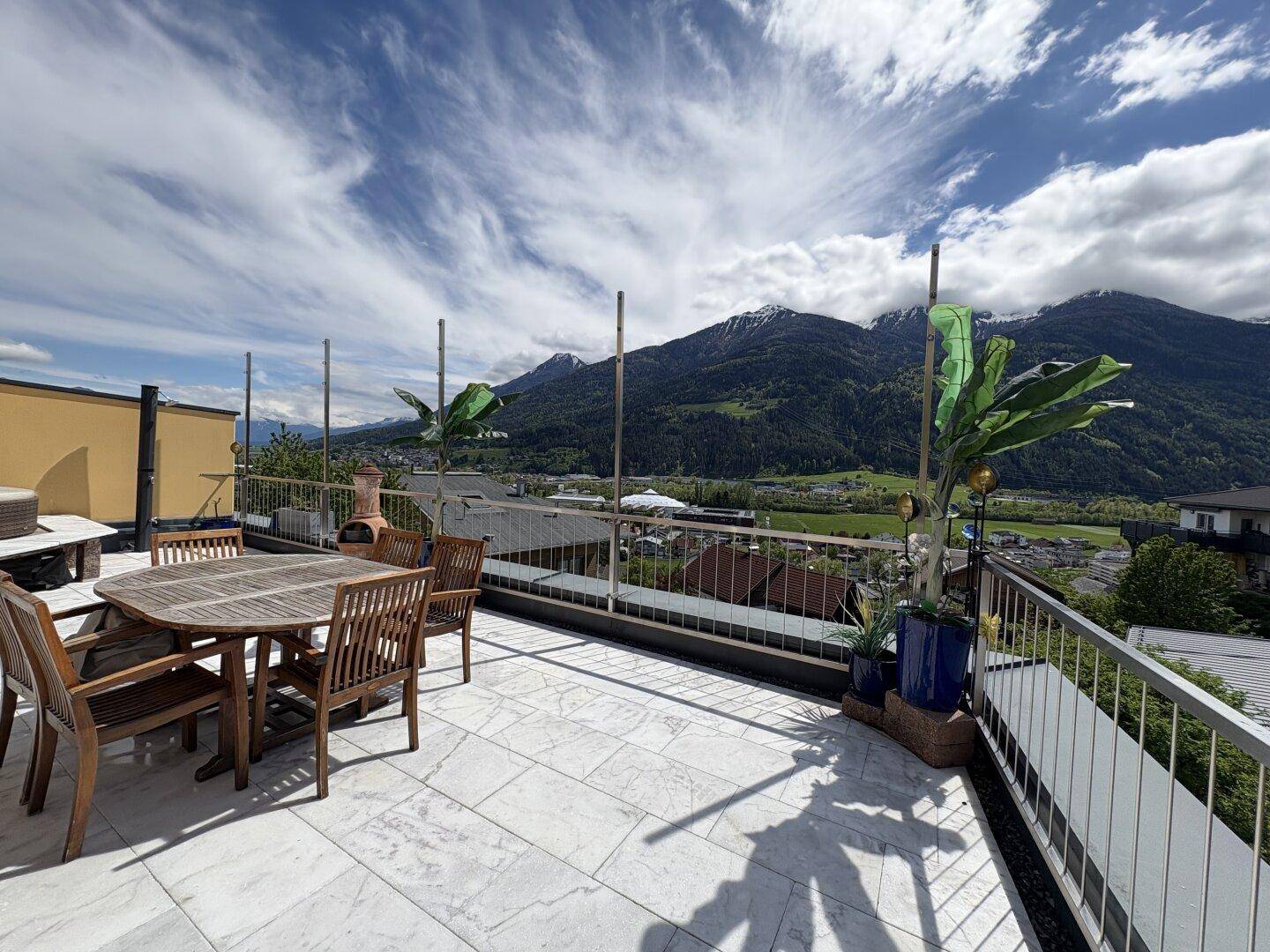 Geräumige Terrasse mit Holztisch, Stühlen und weitem Blick auf die umliegende Berglandschaft.
