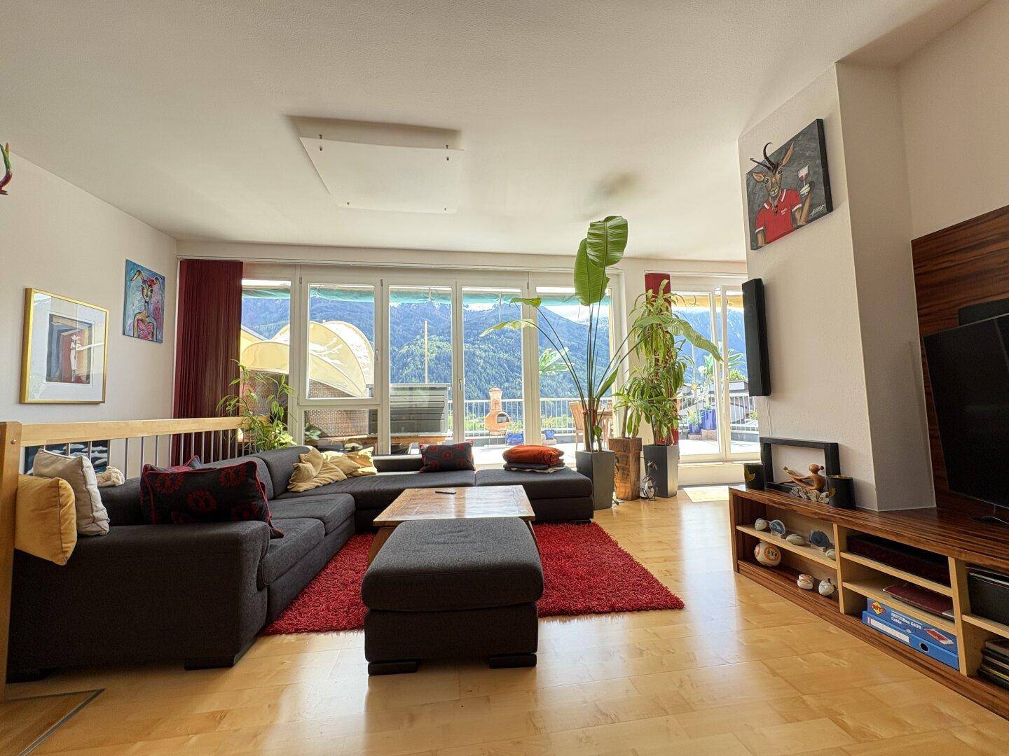 Geräumiges Wohnzimmer mit großem Sofa, Holzboden und Panoramablick auf die Berge.