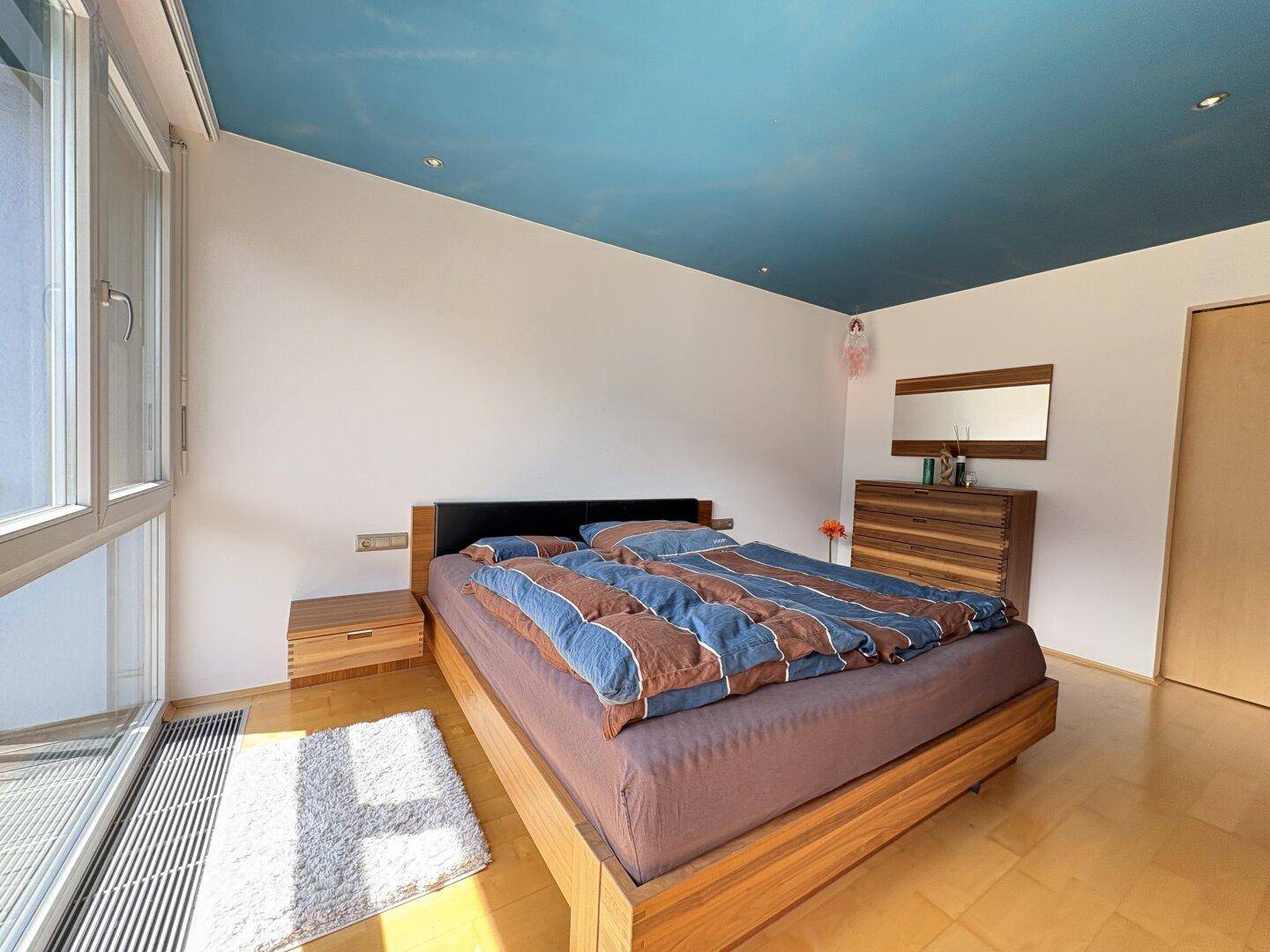 Schlafzimmer mit Holzbett, Holzboden und blauer Decke, hell und einladend.