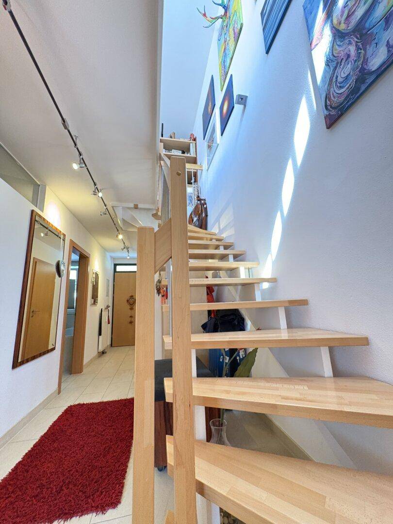 Heller Flur mit Holztreppe, Kunstwerken an der Wand und Blick in den Wohnbereich.