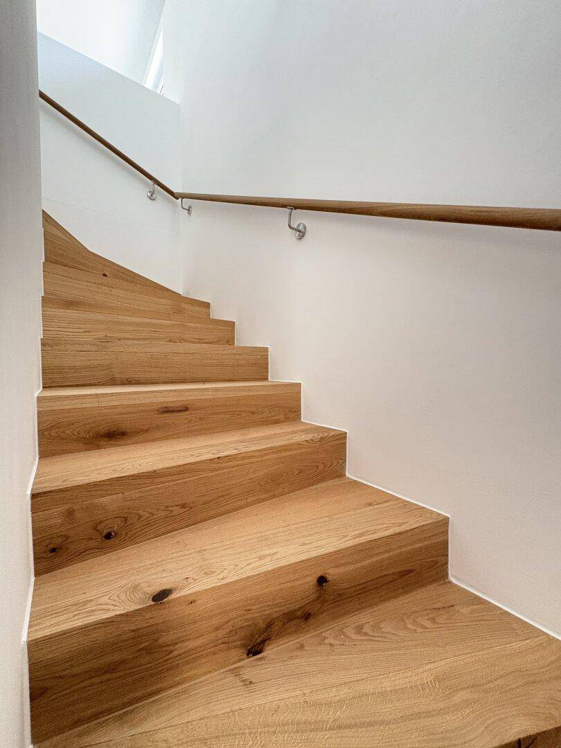 Moderne Holztreppe mit schlichtem Geländer, die verschiedene Ebenen des Hauses verbindet.