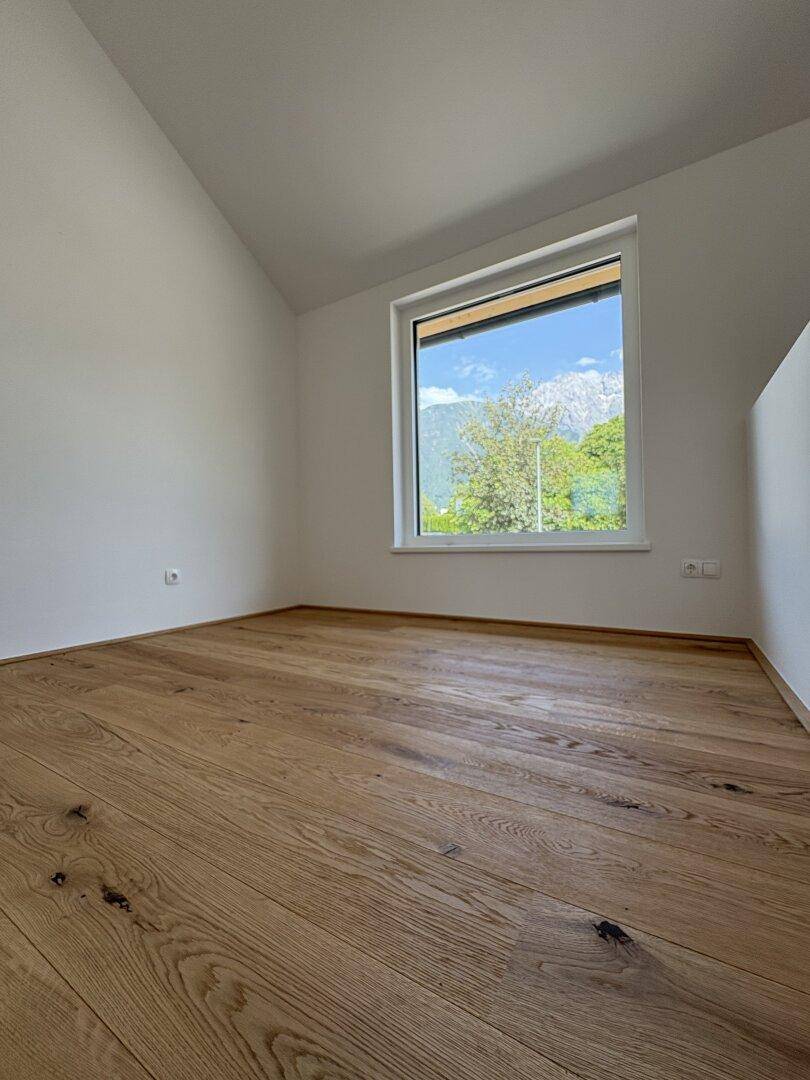 Geräumiges Schlafzimmer mit Holzboden, Dachschräge und Fenster mit Panoramablick auf die umliegende Bergwelt.