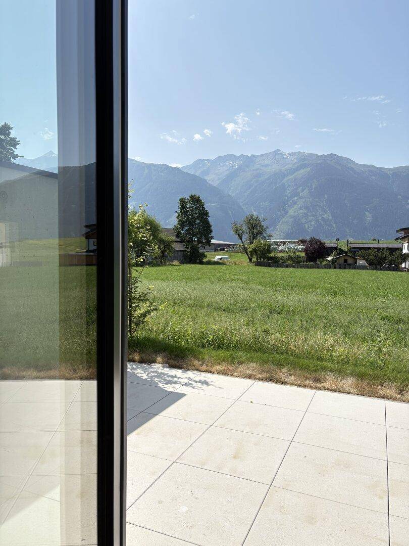 Helle Terrasse mit Fliesenboden und weitem Blick auf grüne Wiesen und Berge.