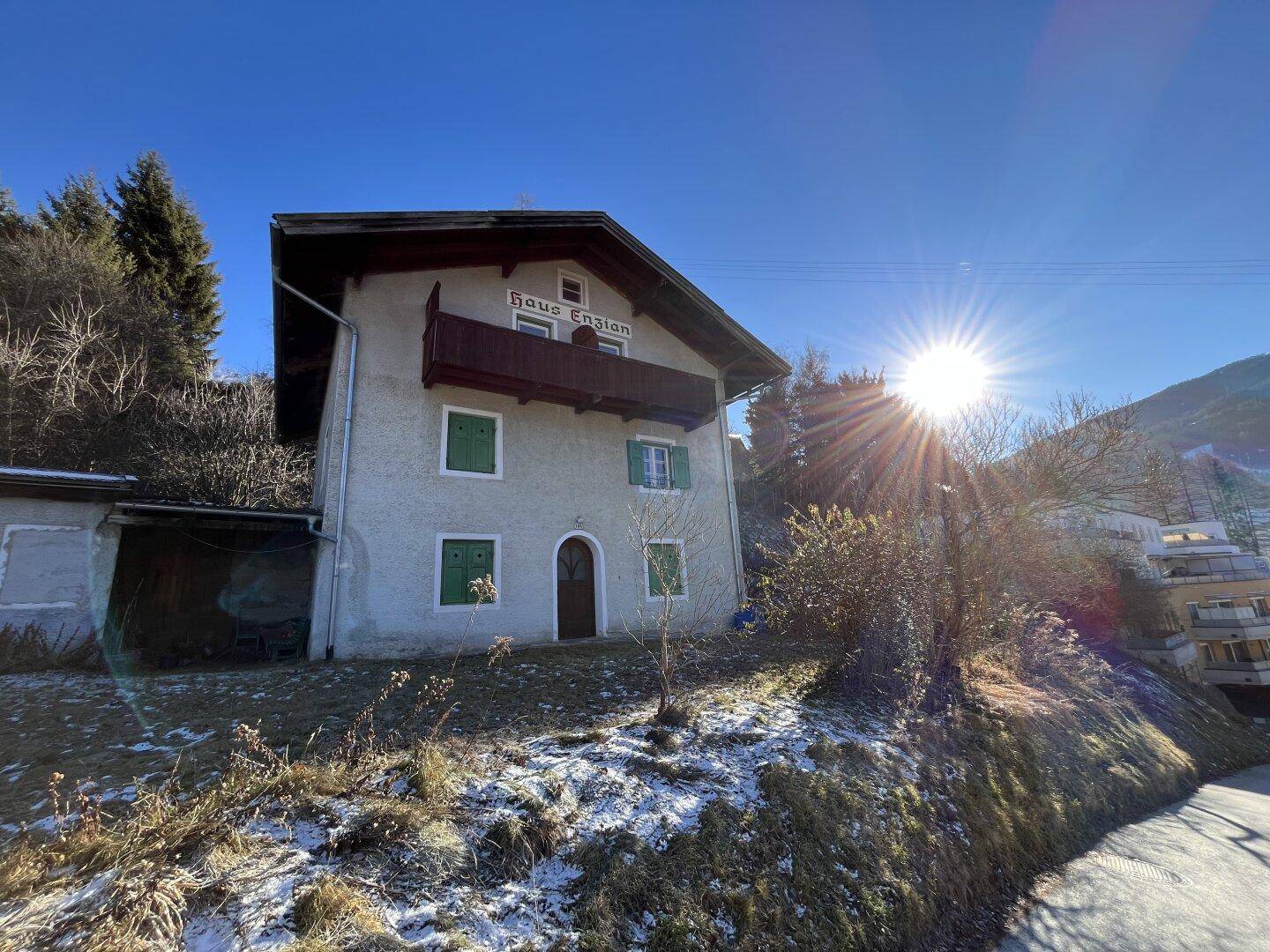 Traditionelles Haus mit Balkon und Satteldach in alpiner Umgebung unter strahlendem Sonnenschein.