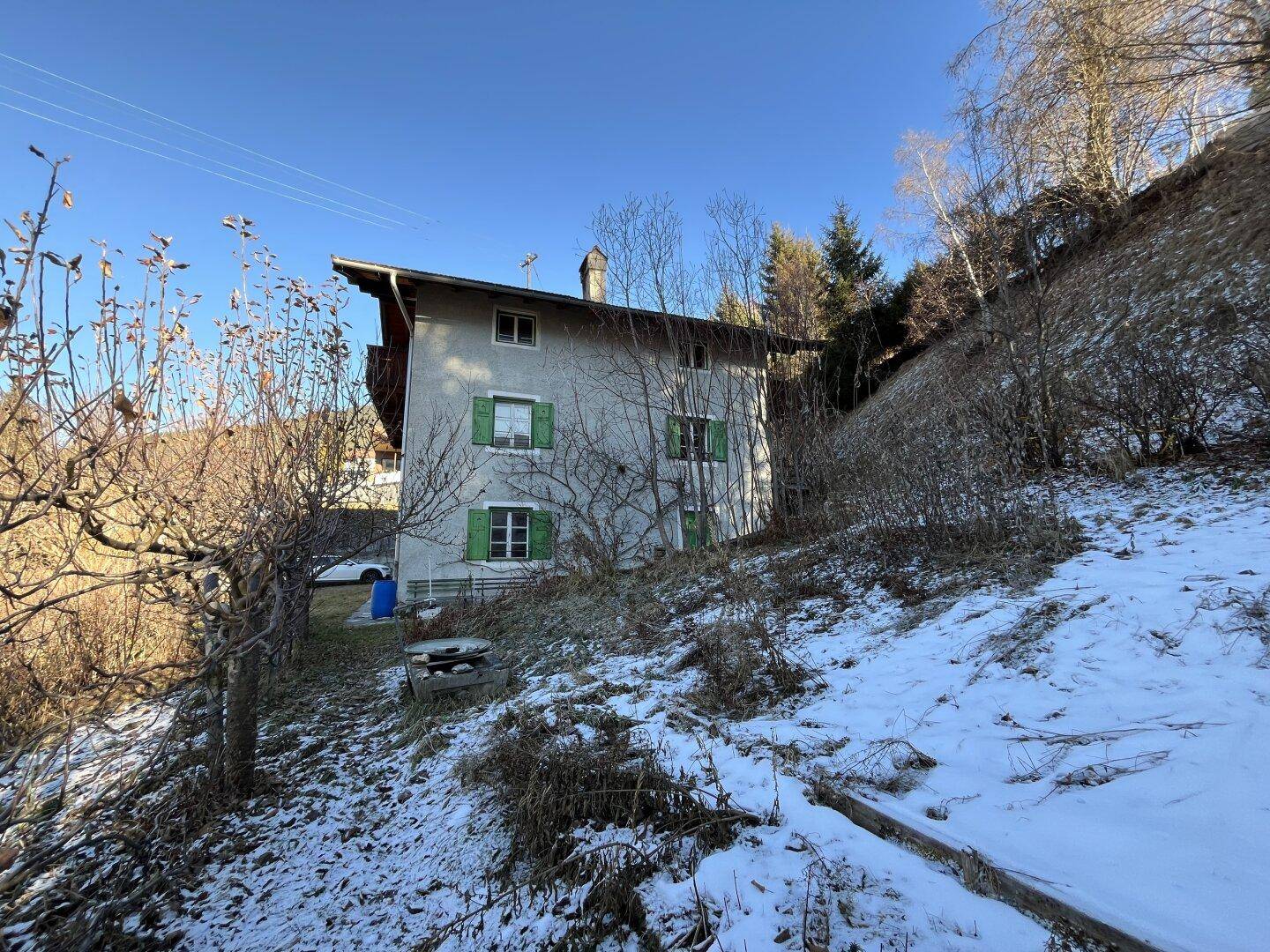 Rückansicht des Hauses mit verschneitem Hang und Bäumen in der winterlichen Berglandschaft.